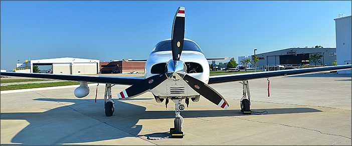 A 2007 Piper Malibu Mirage, a used piston aircraft, is parked on a concrete tarmac in front of several hangars on a clear day.