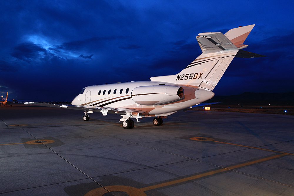A white private jet with tail number N255CX is parked on an airport tarmac at dusk under a cloudy blue sky.