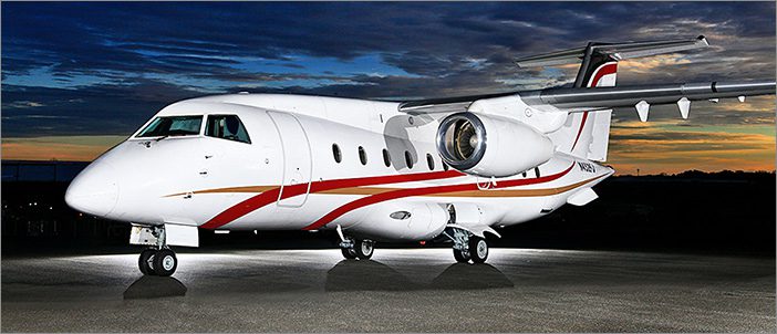 A white and red Dornier 328-300 Jet is parked on a tarmac at dusk, its lights illuminating the 32 passenger commuter aircraft against the dark sky—a striking scene in modern corporate aviation.