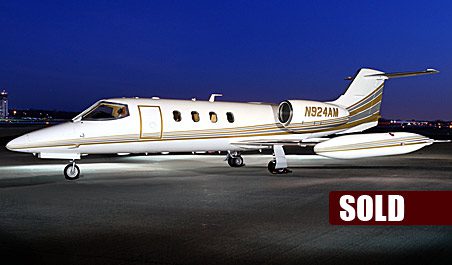 A white and gold private jet is parked on a runway at night; "SOLD" is written in bold letters in the bottom right corner.