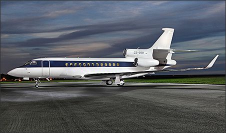 A white and blue 2008 Dassault Falcon7X used business jet is parked on a tarmac at dusk, set against a cloudy sky—an impressive example of corporate aircraft sales.