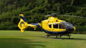 A yellow and blue helicopter is parked on a grassy field with trees in the background.
