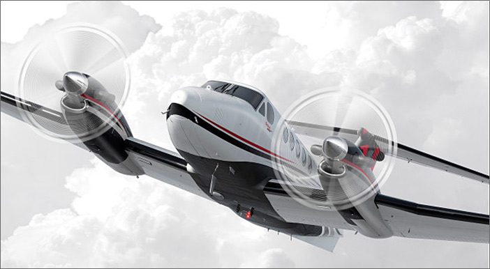 A Beech King Air B200 twin-engine propeller airplane flying in a cloudy sky, viewed from the front left side with both propellers in motion—perfect for those seeking quality used aircraft for sale.