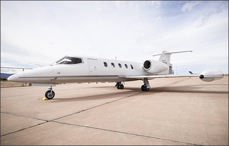 A white Lear 35A for sale is parked on a concrete runway under a cloudy sky, showcasing the sleek design of this used Lear aircraft jet.