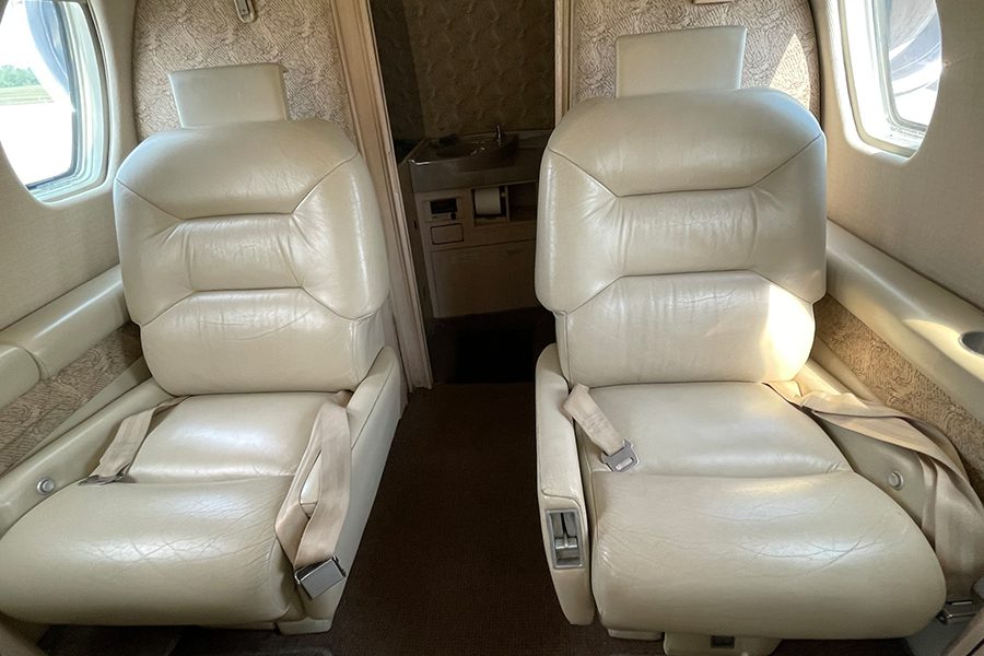 Two white leather seats in an airplane.