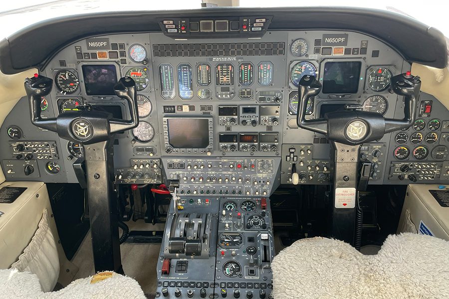 Cockpit view of an aircraft showing dual control yokes, numerous gauges, switches, and instrument panels on the dashboard.