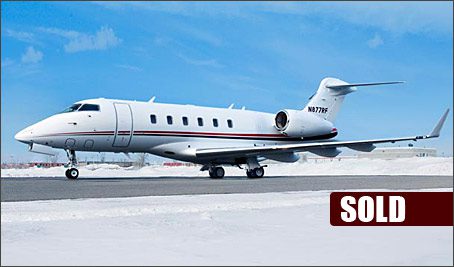 A white Challenger 300 private business jet sits on a snowy tarmac under a blue sky. A "SOLD" label is visible in the lower right corner.