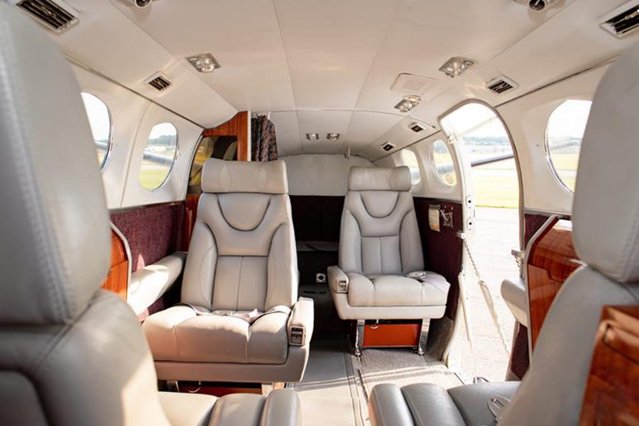 The interior of a small private airplane with four grey leather seats, wood paneling, side windows, and natural light coming in.
