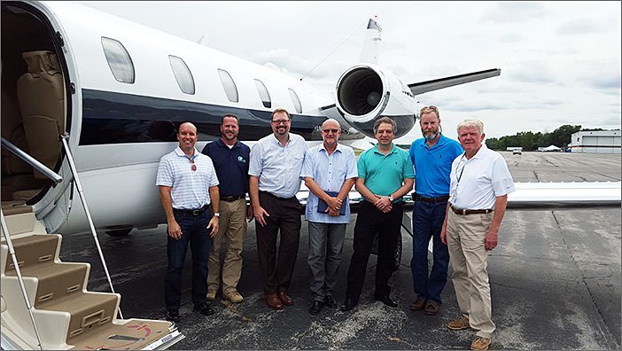Seven men stand on an airport tarmac in front of a private jet, posing for a group photo after a successful Citation Excel acquisition, showcasing expertise in general aviation services.