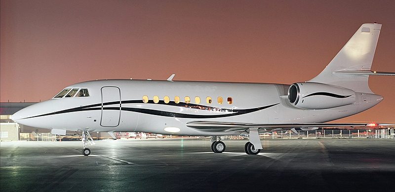 A sleek white private jet with black and gray accents is parked on an airport tarmac at night, illuminated by nearby lights.
