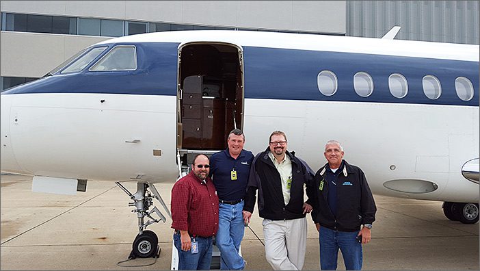 Four men stand smiling in front of a sold 2003 Falcon 2000 on an airport tarmac, highlighting successful used corporate jet sales and general aviation services.