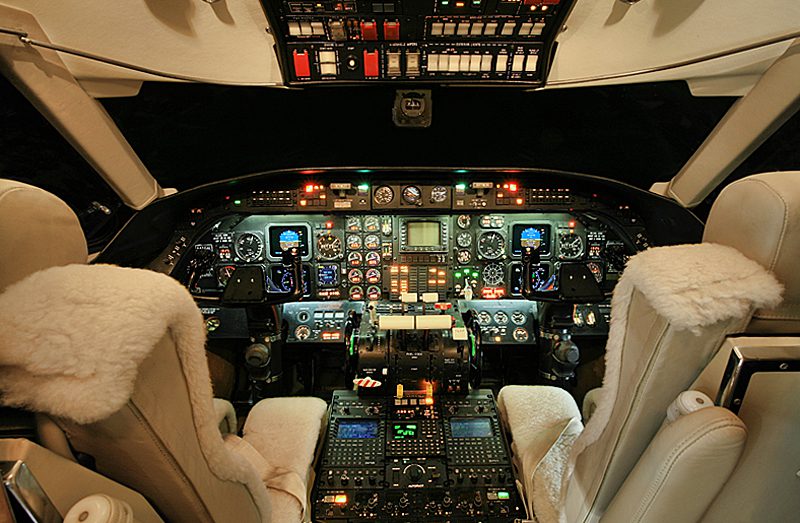 Cockpit of an aircraft with two cream-colored pilot seats and an array of illuminated flight instruments, gauges, and control panels.