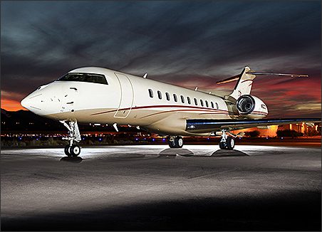 A Bombardier Global 5000 used corporate jet for sale, with red and gold accents, is parked on a runway at dusk, set against a colorful sunset backdrop.