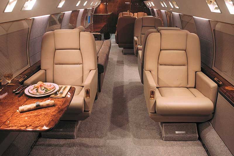 Interior of a private jet with beige leather seats, wood-paneled tables, and a meal served on a plate on one of the tables.