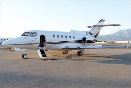 A white used Hawker 700A with an open door and stairs is parked on an airport tarmac, with mountains visible in the background.