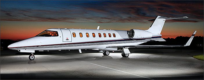 A white Learjet 45 used business jet is parked on a runway at dusk, its sleek silhouette framed by orange and blue hues, available through General Aviation Services broker.