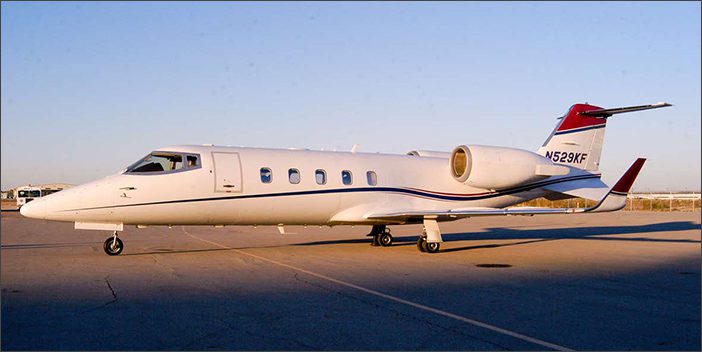 A white Learjet 60 with the registration number N529KF, a sleek corporate aircraft, is parked on an airport tarmac under a clear sky.