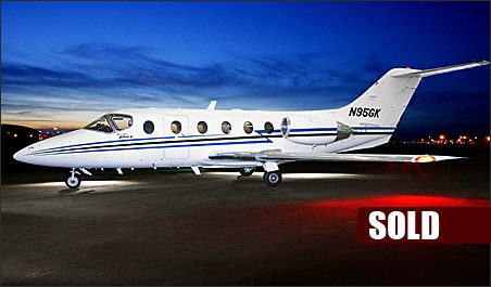 A white Beechjet 400A with blue stripes is parked on a runway at dusk, with a "SOLD" label in the lower right corner—showcasing the demand for used Beechjet 400A aircraft.