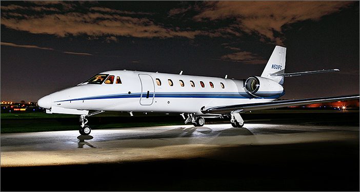 A used Citation Sovereign 608-0107 business aircraft with blue stripes is parked on an airfield at night, spotlights highlighting this impressive corporate jet.