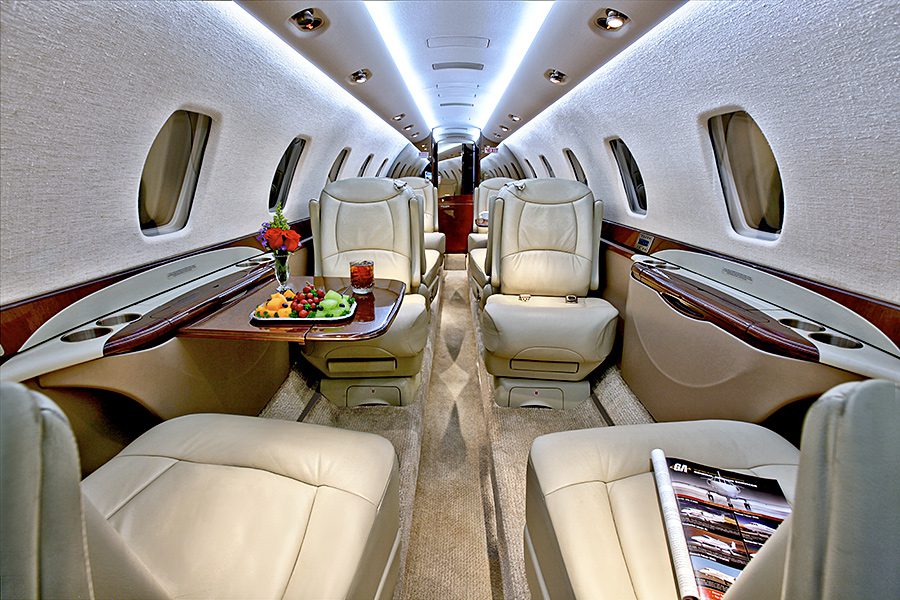 Interior of a private jet with cream leather seats, a tray of snacks and drinks on a table, and a magazine on one seat, showing a luxurious cabin setting.