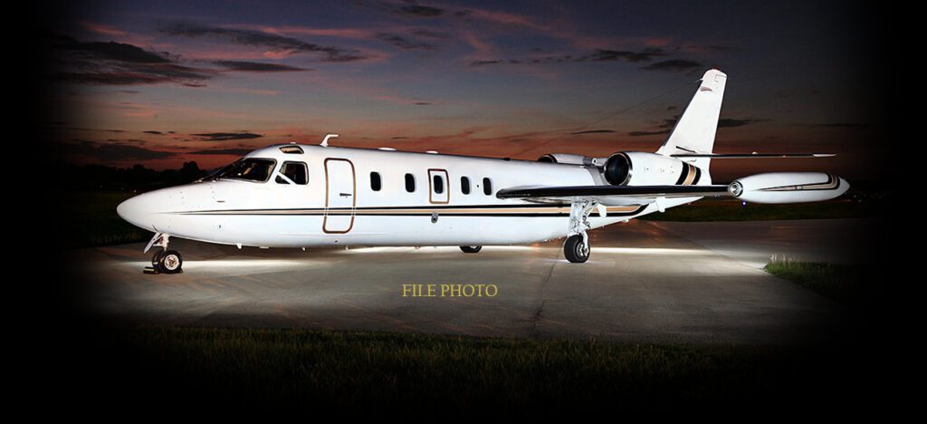 A white business jet is parked on a runway at dusk under a dark sky with clouds. The words "FILE PHOTO" appear near the bottom center of the image.