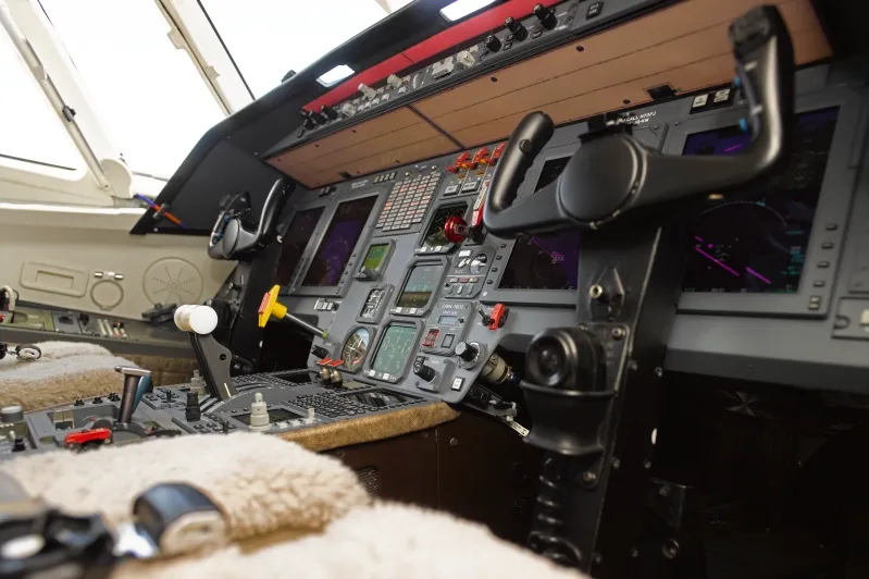 Close-up view of an airplane cockpit featuring flight control yokes, instrument panels, switches, and various controls.