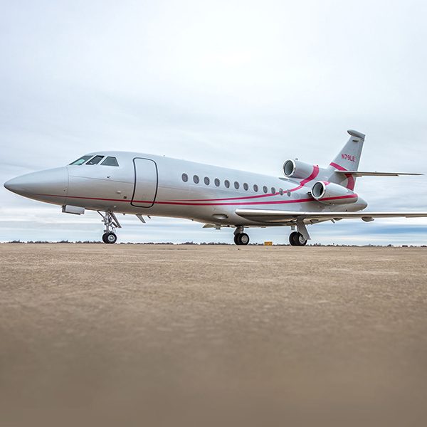 A white private jet with red accents is parked on an empty tarmac under an overcast sky.