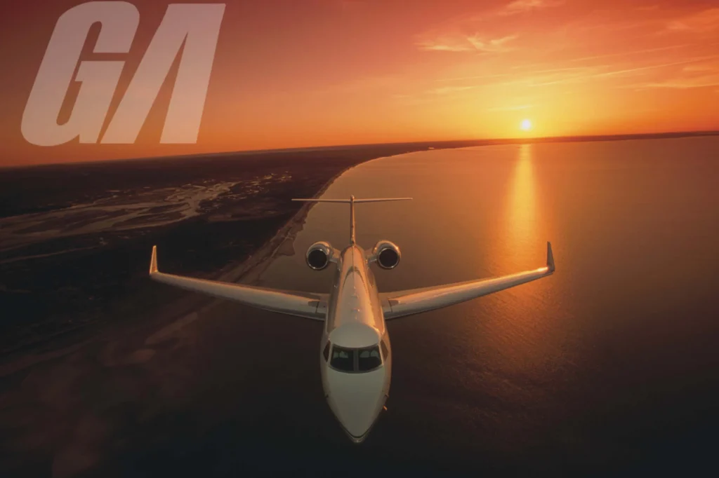 A private jet flies over a coastline at sunset, reflecting on the water with an orange sky. Large "GA" text appears in the top left corner.