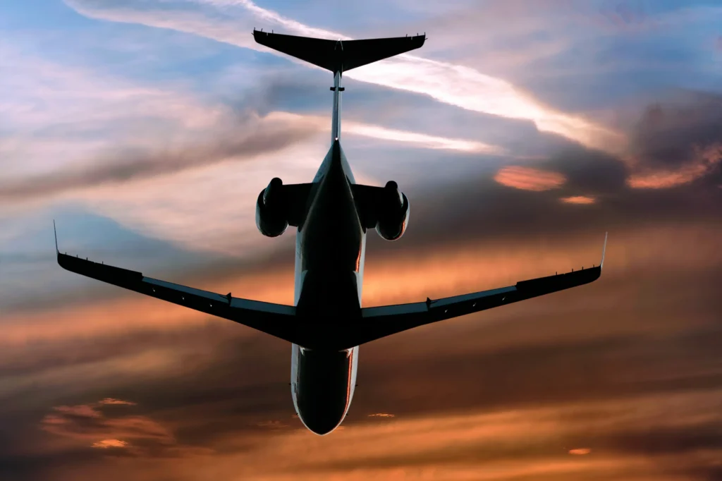 Silhouette of a commercial airplane flying overhead against a dramatic sunset sky with clouds.