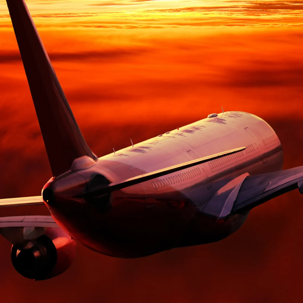 A commercial airplane flying above the clouds during sunset, with the sky colored in shades of orange and red.