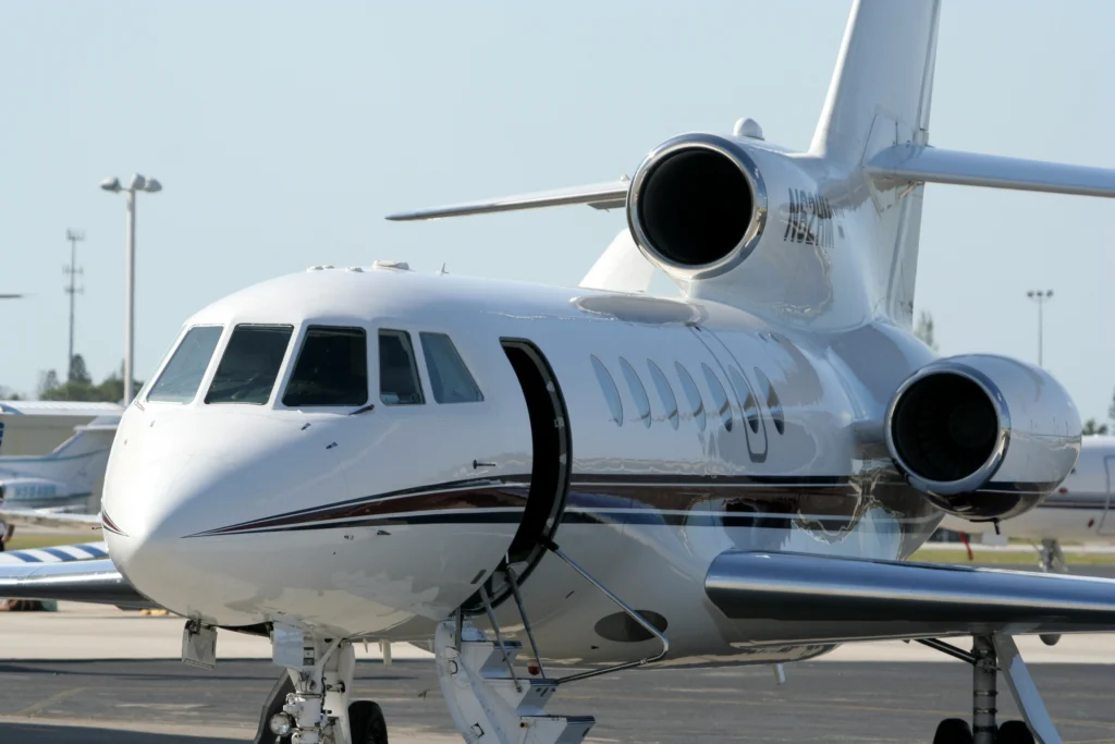 A white private jet with its door open is parked on an airport tarmac during the day.