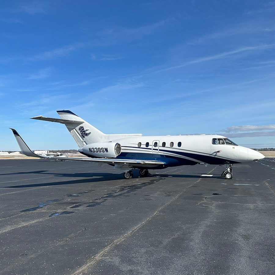 A white and blue Hawker 800A private jet with the registration number N329SN is parked on an airport tarmac under a clear blue sky.